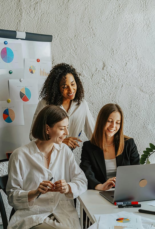 groupe de 3 femmes en pleine réunion elles sourient en regardant l'écran de leur ordinateur